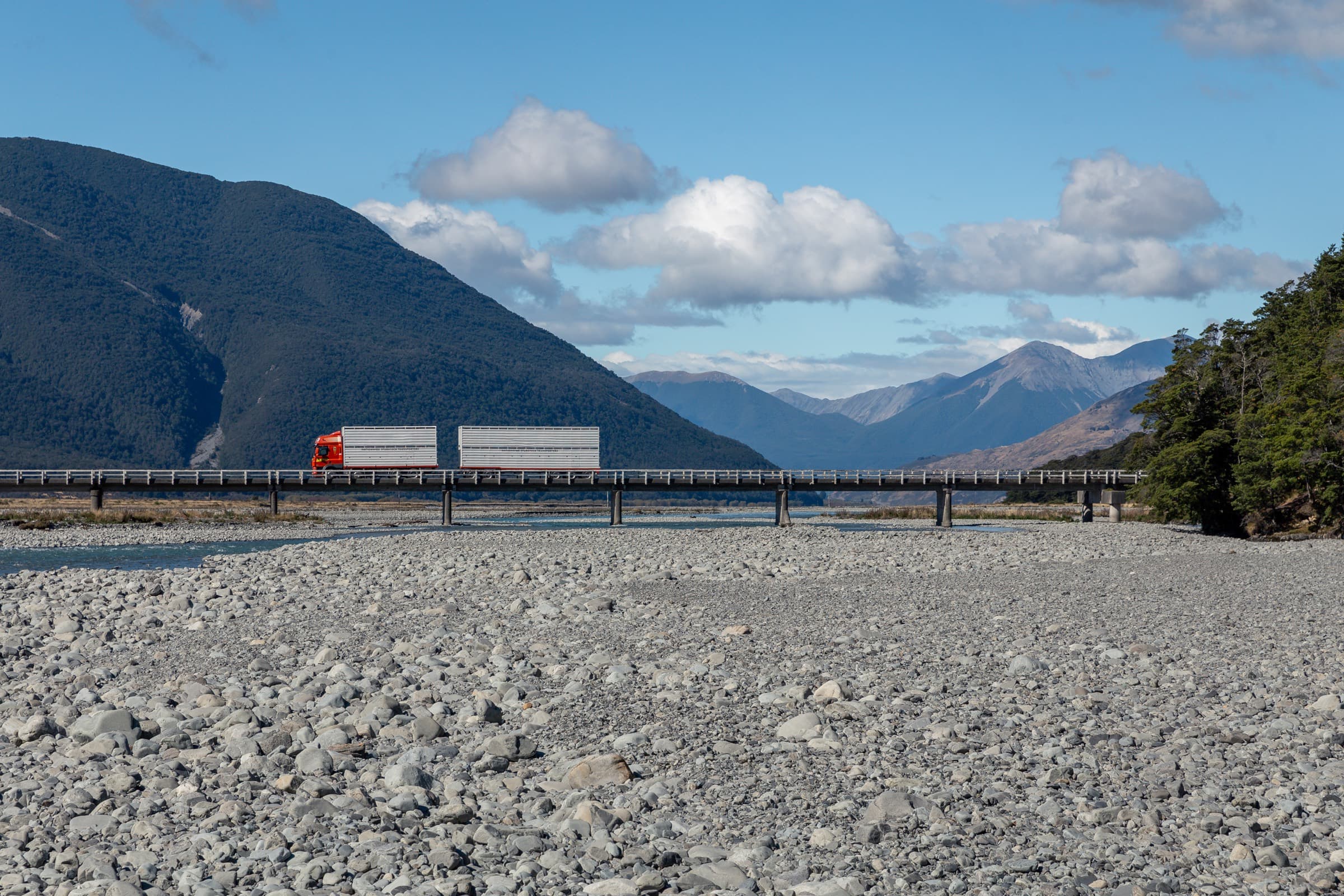 A stock truck and trailer crossing a river bridge on a New Zealand highway